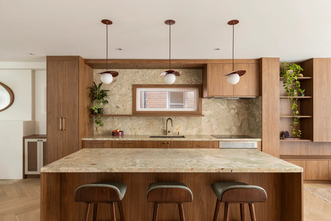Walnut kitchen with a stone-topped island, stone backsplash and three pendant lights