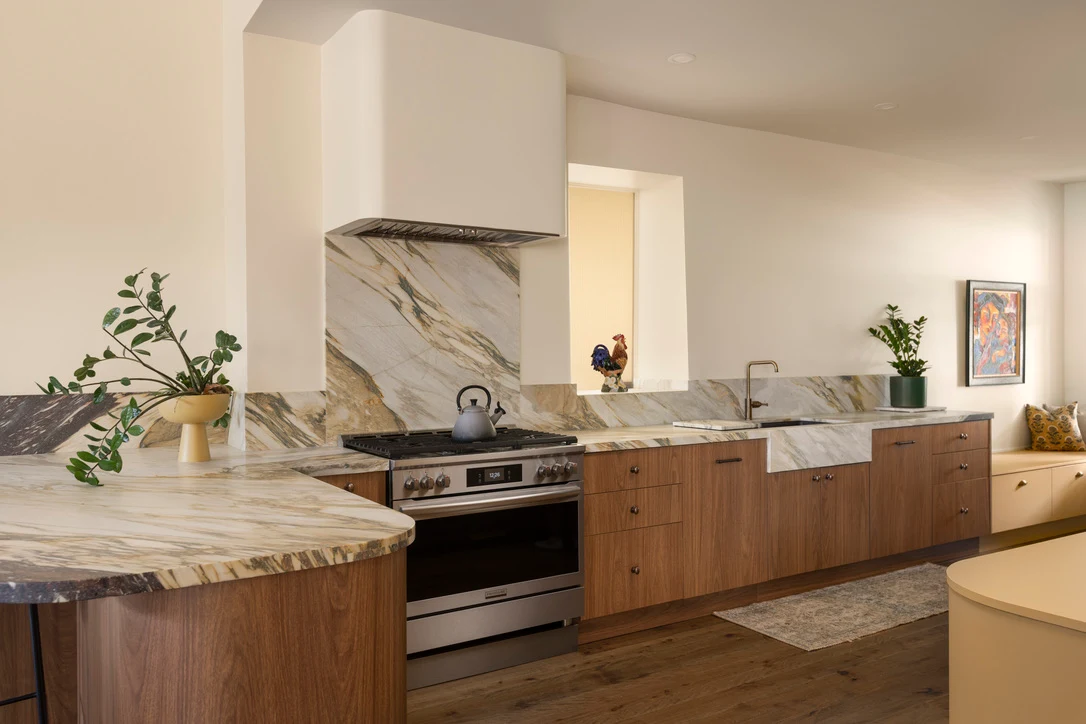 Walnut kitchen cabinets with a marble backsplash and a curved marble-top peninsula