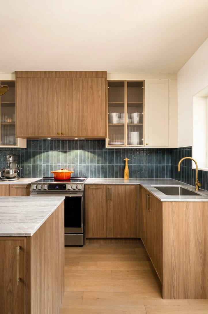 L-shaped walnut kitchen with teal tile backsplash, glass-front cabinets and a brass faucet