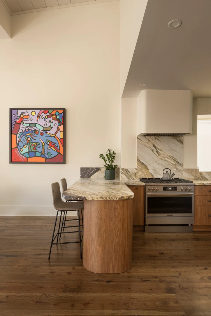 Rounded walnut kitchen peninsula with a marble counter and bar stools beside a gas range