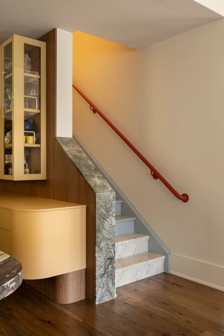 Curved yellow cabinetry and glass display cabinet beside a marble-clad staircase