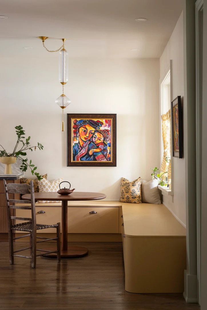 Built-in yellow banquette seating in a bright breakfast nook with a pedestal table