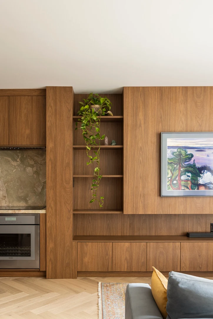 Floor-to-ceiling walnut wall unit with open shelves, a built-in oven and a low media console