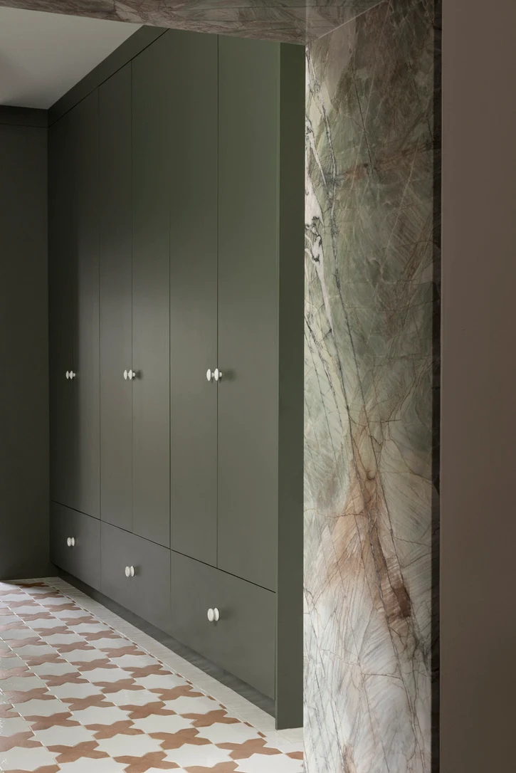 Olive green built-in wardrobe with drawers next to a green marble wall surround