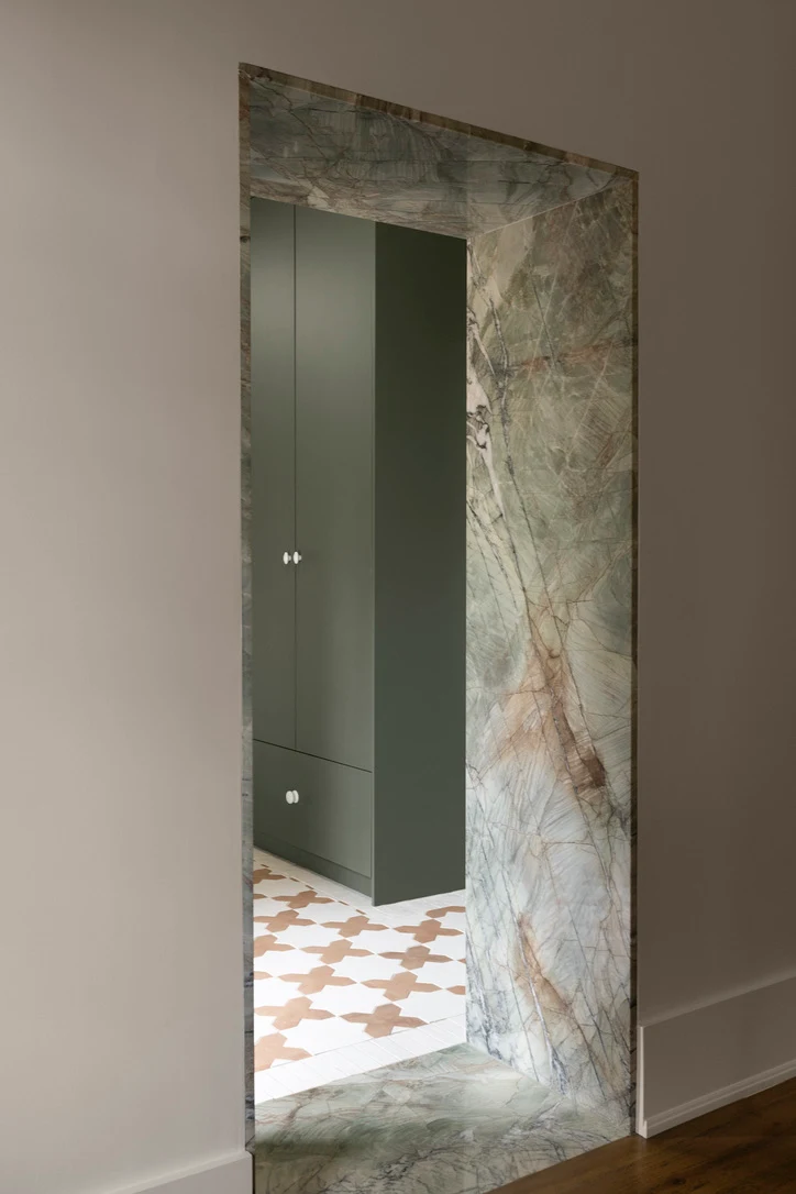 Marble-framed doorway opening to olive green built-in cabinetry and a patterned tile floor