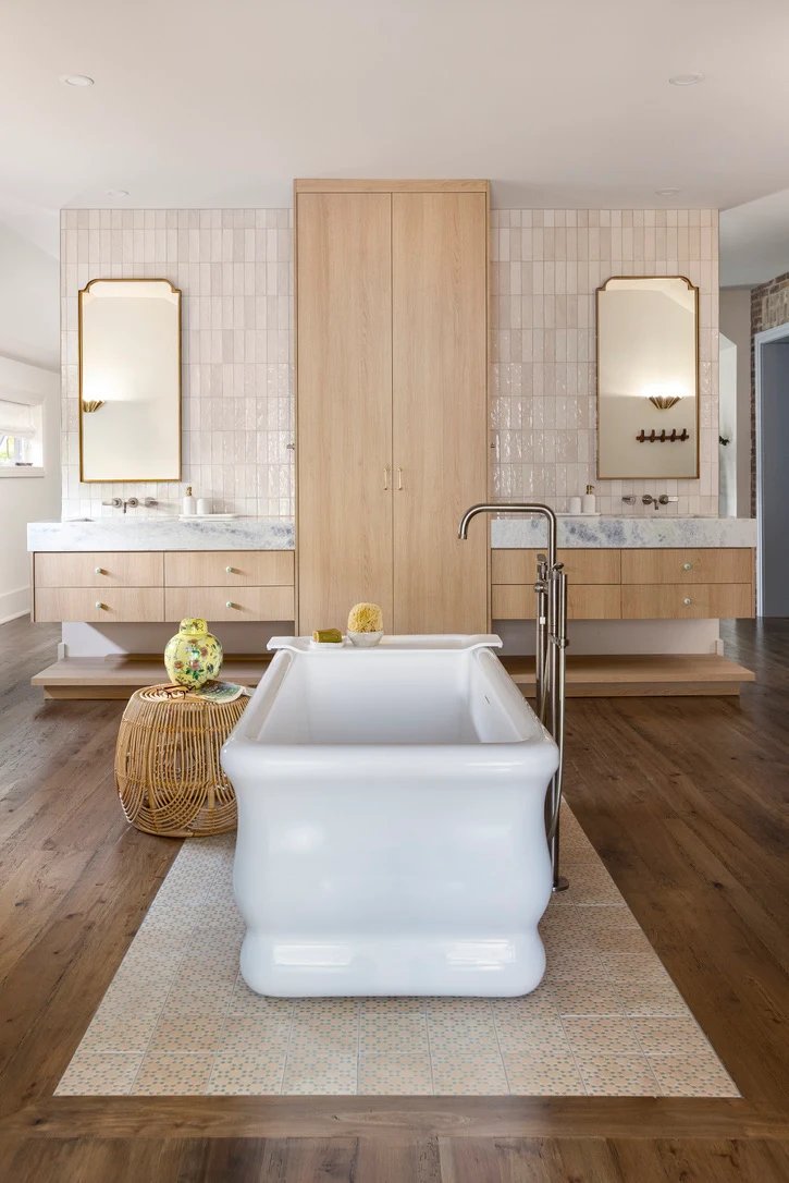 Primary bathroom with two oak floating vanities, a tall oak storage cabinet and a freestanding tub