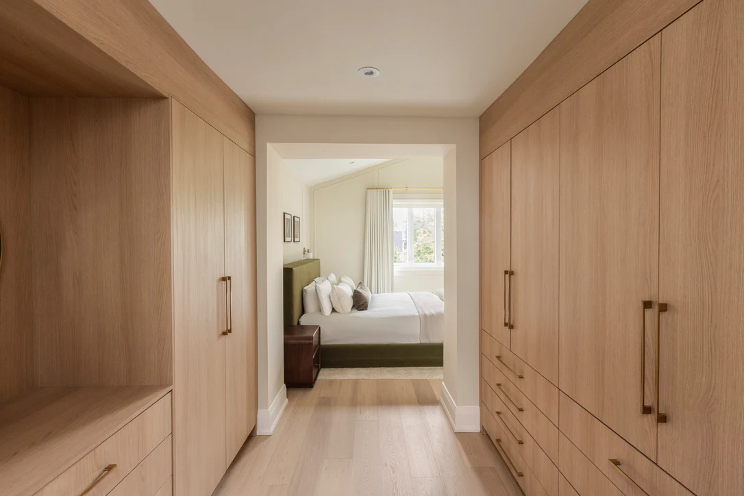 White oak walk-in closet with brass pulls, open shelving and drawers leading to a bedroom