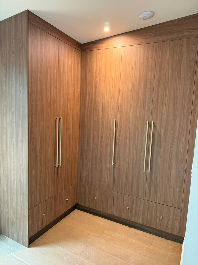 Walnut corner wardrobe with tall brass handles, lower drawers and wood-grain doors