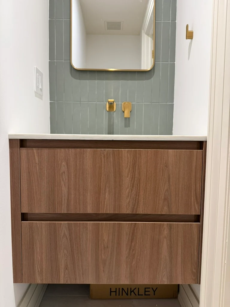 Floating walnut vanity with two drawers, brass wall-mounted faucet and a gold-framed mirror
