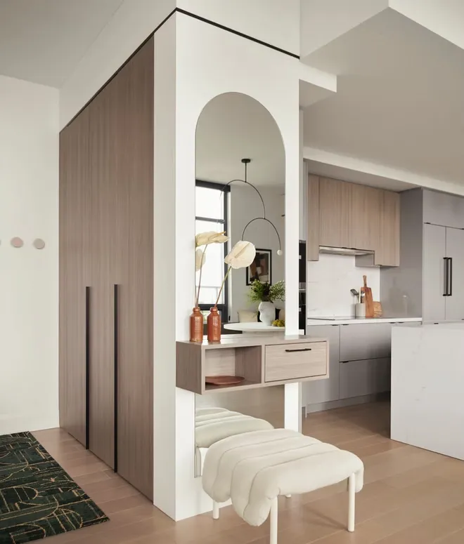 Wood-grain wardrobe tower beside an arched mirror, a floating shelf and an upholstered bench