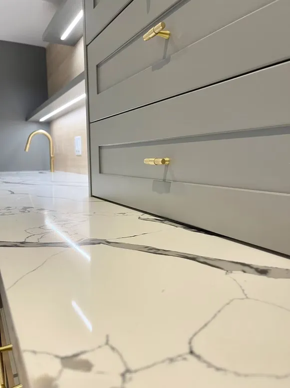 Close-up of grey shaker drawer fronts with brass knobs above a white marble-look countertop