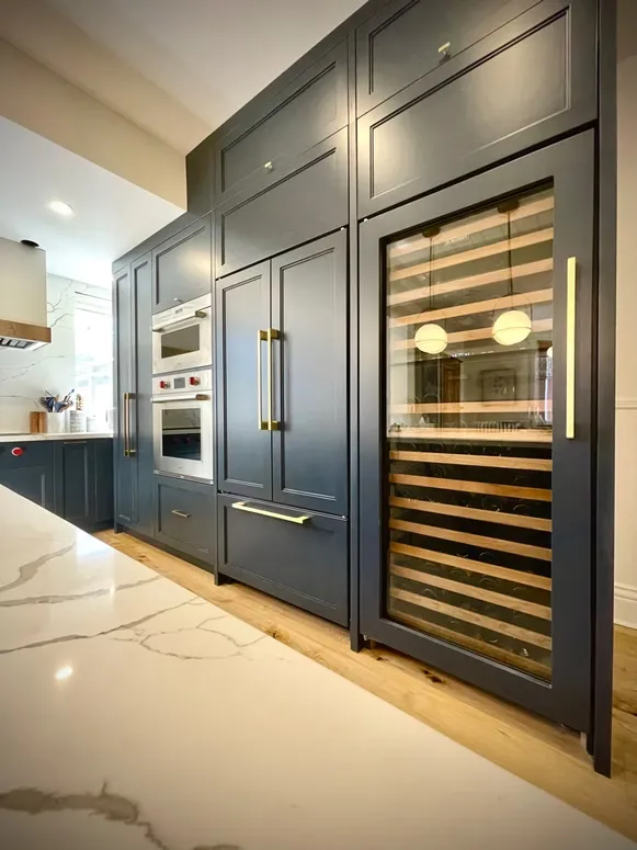 Navy blue kitchen wall with a panelled refrigerator, double wall ovens and a wine cooler with brass handles