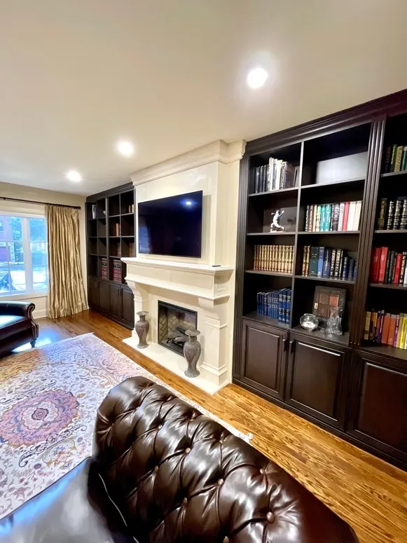 Traditional living room with dark stained built-in bookcases around a white fireplace mantel and TV