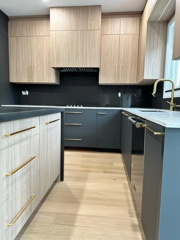 Kitchen with light wood-grain cabinets, charcoal base cabinets, a black backsplash and brass bar pulls