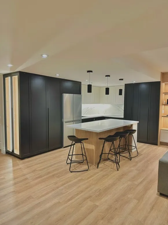 Open kitchen with black tall cabinets, a ribbed-front island with bar stools and wood floors