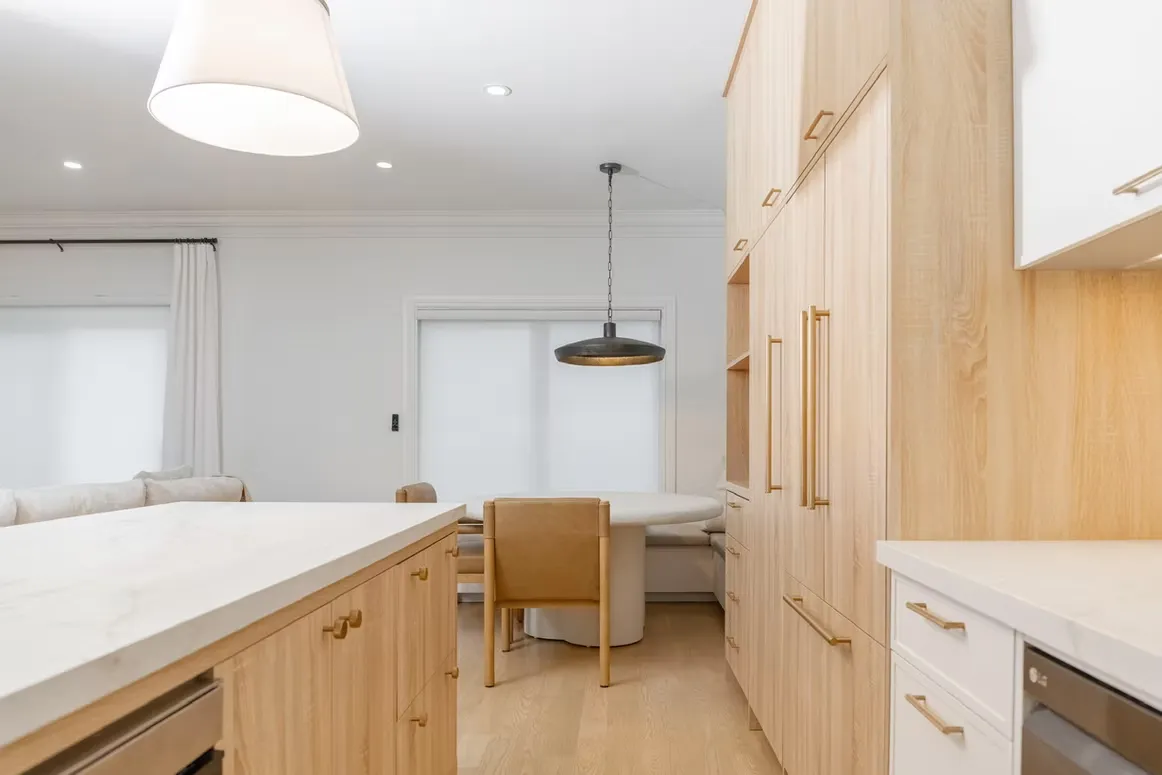 Light oak kitchen with a panelled refrigerator, an island with brass pulls and a dining area behind