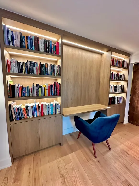 Built-in oak bookcases with integrated lighting and a floating desk with a blue accent chair