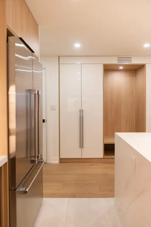 Kitchen corner with a stainless steel fridge, white tall pantry doors and an oak-lined bench niche