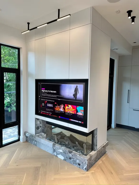 Three-sided gas fireplace with a built-in TV in a white fluted cabinet wall over a herringbone floor