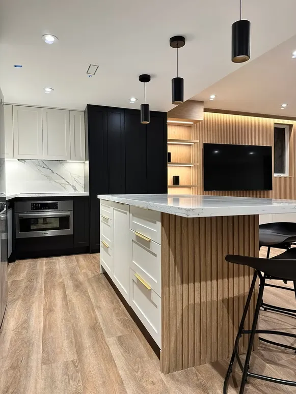 Kitchen with a fluted-front island, white shaker drawers with brass pulls and a black tall cabinet