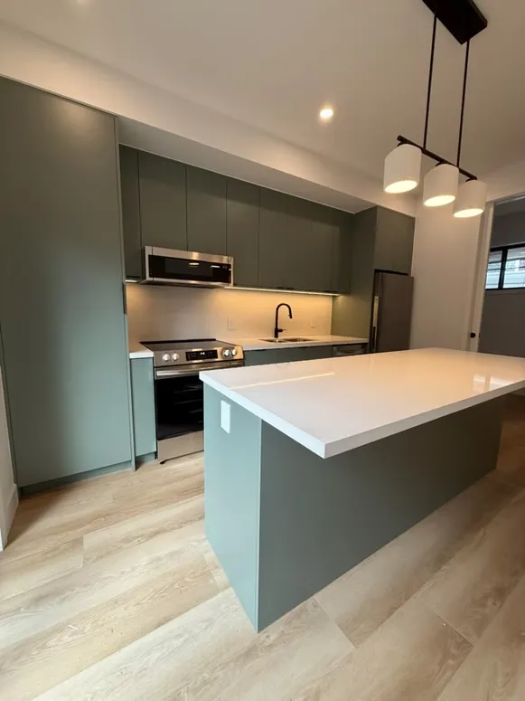 Sage green kitchen with a matching island, a white quartz top and a three-light pendant