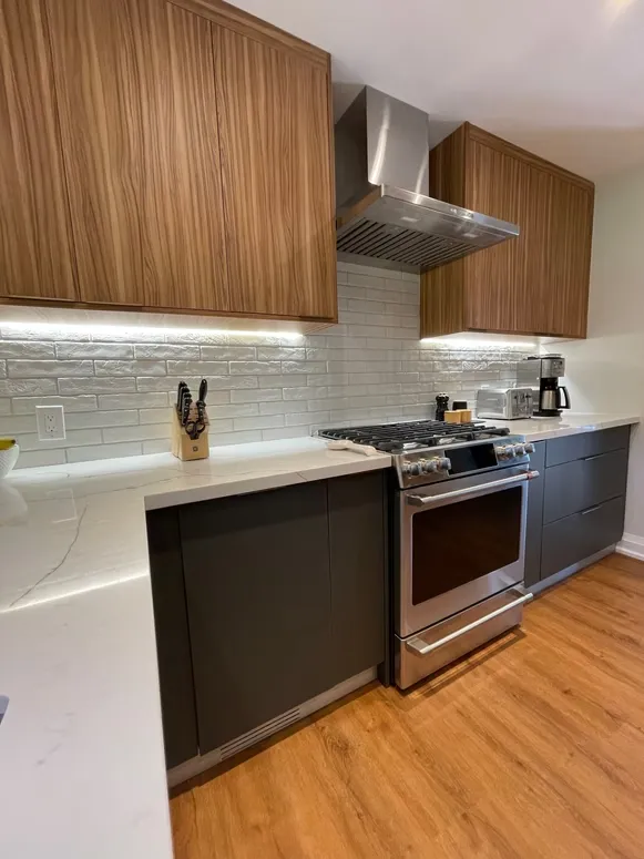 Kitchen with walnut upper cabinets, charcoal base cabinets, a stainless range and under-cabinet lighting