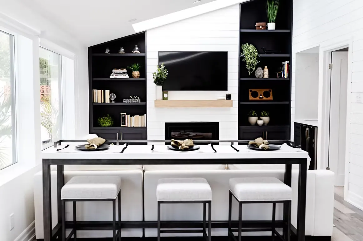 Living room with black built-in shelving around a white fireplace and a console table with stools