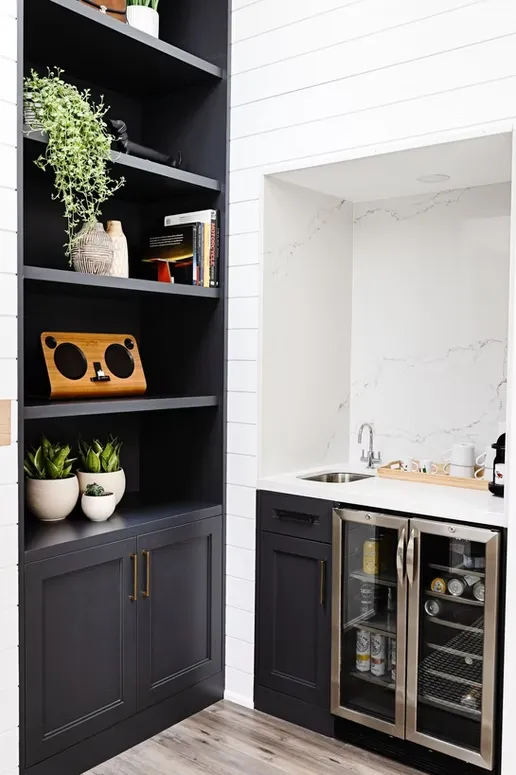 Black built-in shelving next to a wet bar niche with a beverage fridge and a marble-look backsplash