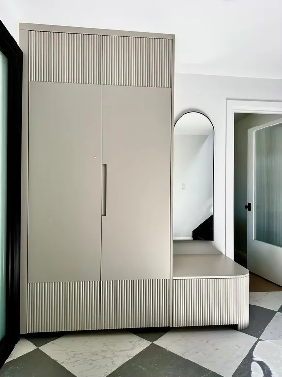 Greige entry cabinet with fluted details and a curved bench beside a checkerboard tile floor