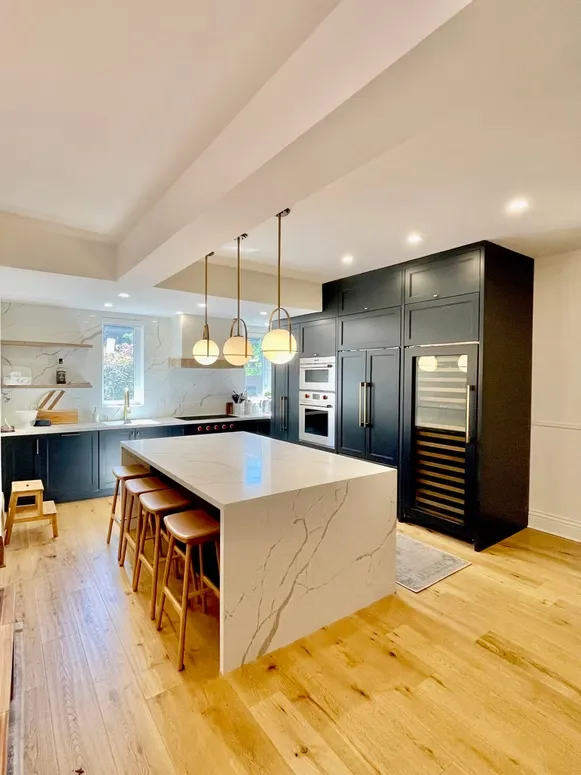 Navy kitchen with a marble-look waterfall island, a wine cooler and built-in ovens