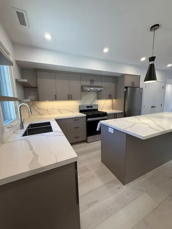 Taupe kitchen with a veined quartz countertop, an island and under-cabinet lighting