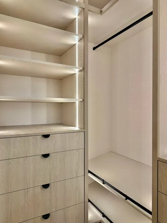 Walk-in closet with lit open shelves, drawers with black pulls and a hanging rail