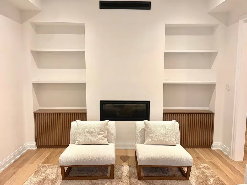 Living room with white built-in shelves and slatted cabinets on both sides of a linear fireplace