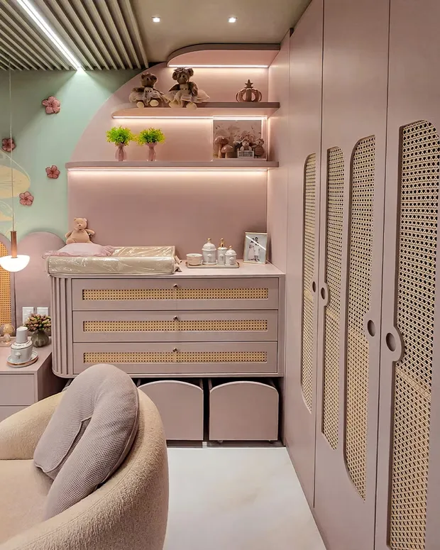 Nursery with a pink built-in changing dresser, cane-front wardrobe doors and lit shelves