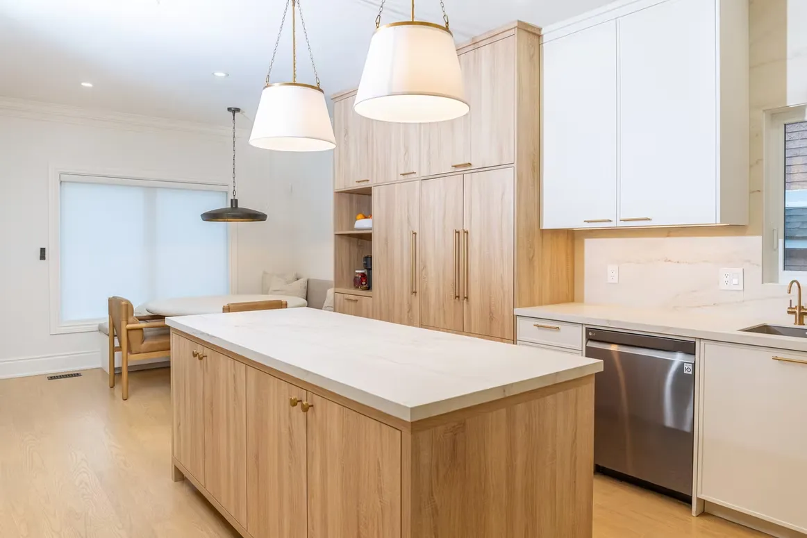 Light oak kitchen with an island, tall oak pantry cabinets and two drum pendant lights