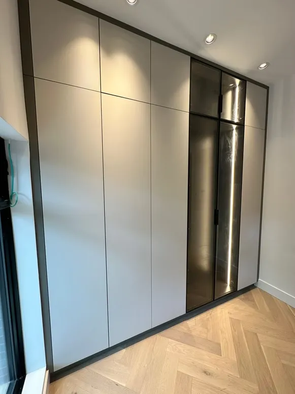 Floor-to-ceiling grey wardrobe with black-framed smoked glass doors on a herringbone floor