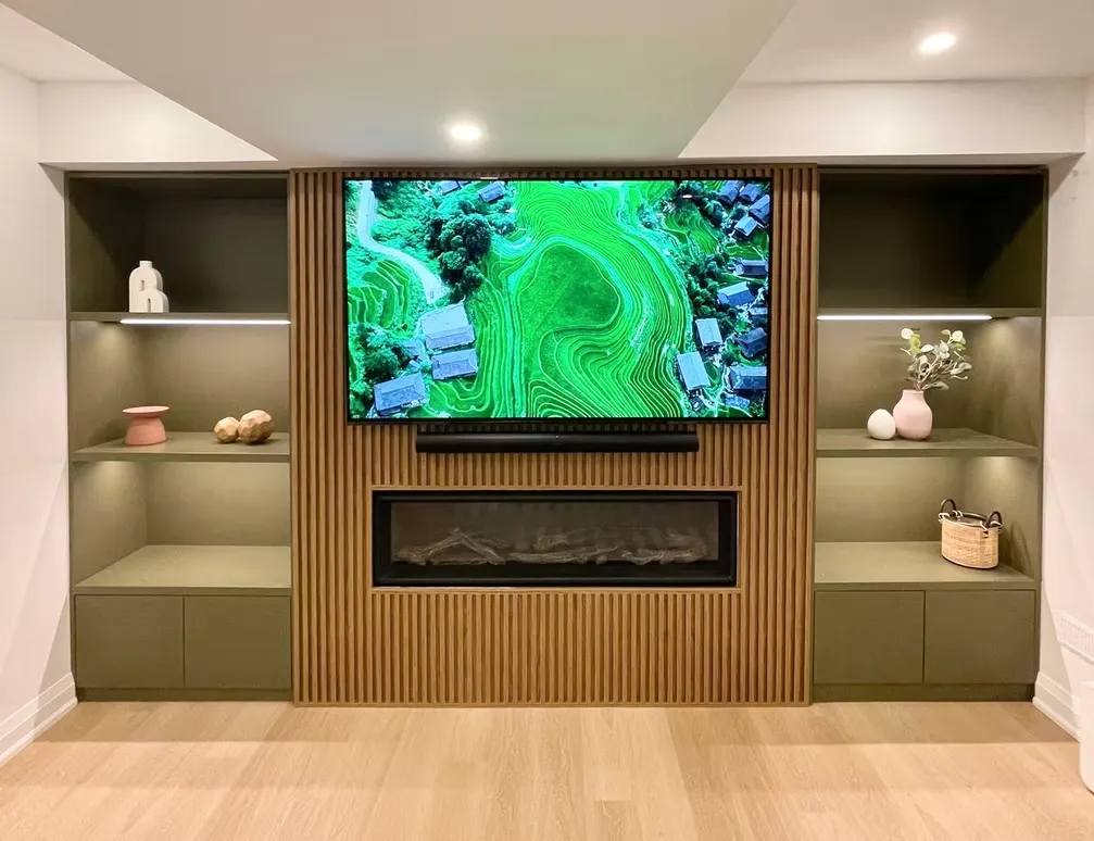 Built-in media wall with olive green shelves, a slatted wood panel, a TV and a linear fireplace