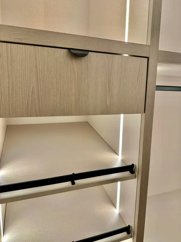 Close-up of a closet drawer with a finger pull, lit shelving and a black hanging rod