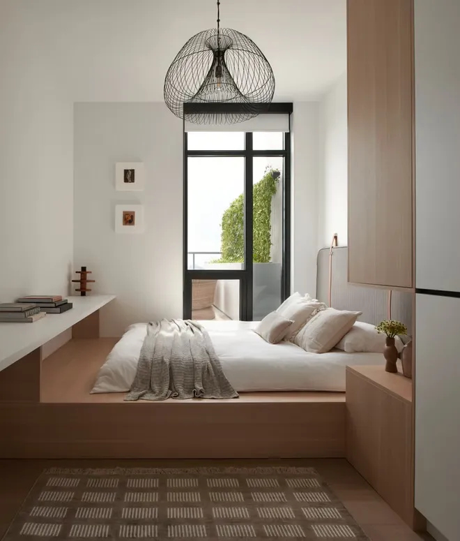 Bedroom with a raised oak platform bed, built-in oak storage and a wire pendant light