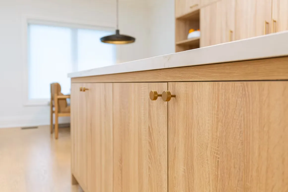 Close-up of light oak kitchen cabinets with brass knobs under a white countertop