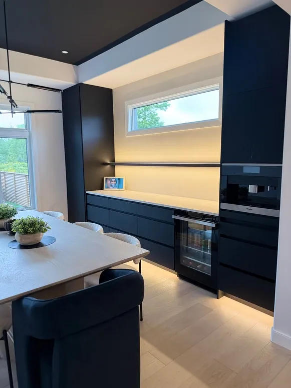 Navy built-in cabinetry with a coffee machine, an oven and warm lighting beside a dining table