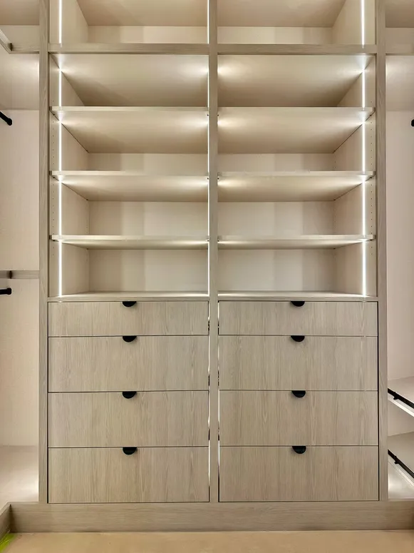 Walk-in closet with lit shelves and two stacks of oak-look drawers with black finger pulls