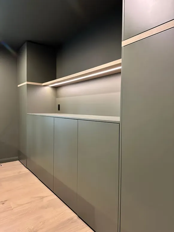 Sage green built-in cabinetry with a lit oak-edged shelf in a dark green room