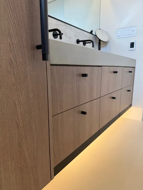 Floating oak vanity with black handles, under-cabinet lighting and black wall faucets
