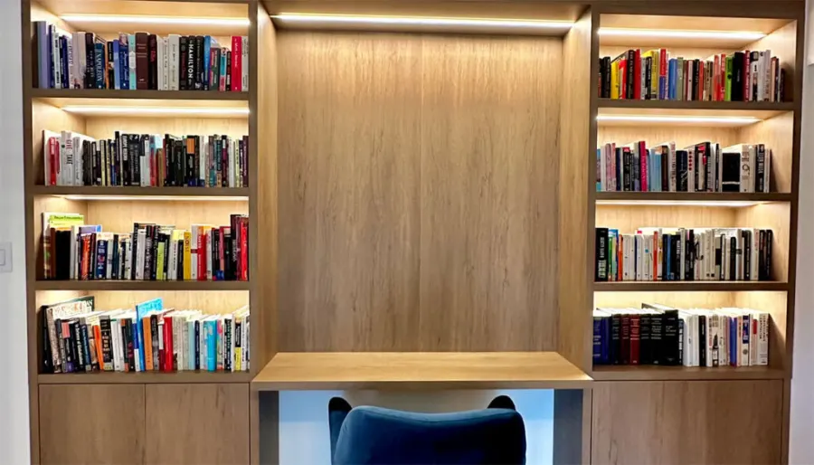 Home office built-in with lit bookshelves and a desk by VIVA Cabinetry