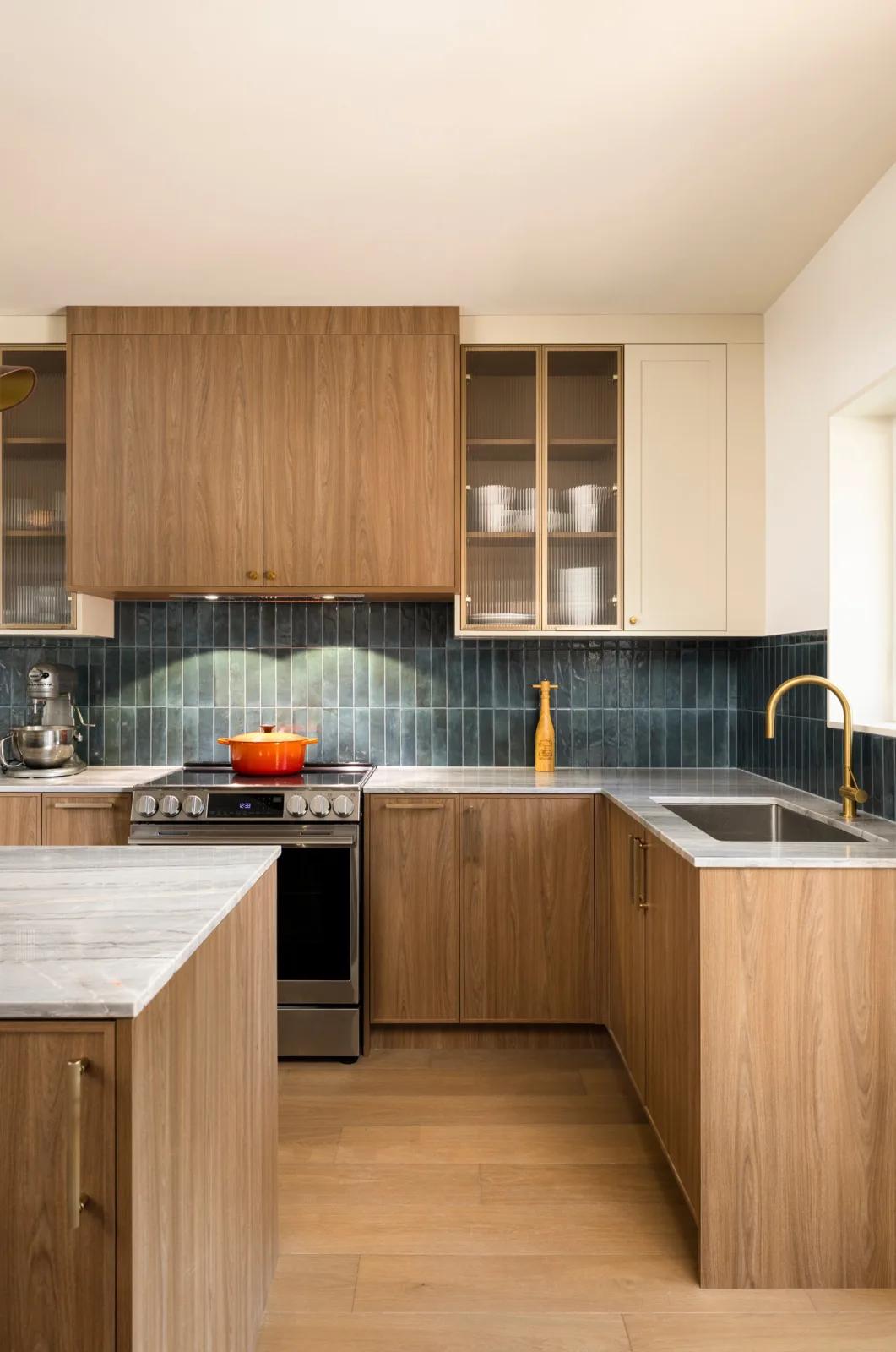 Walnut kitchen cabinets with fluted glass uppers, blue tile backsplash and brass hardware, installed by VIVA Cabinetry
